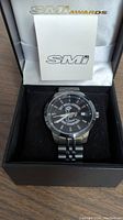 Men's wristwatch in black dial and silver metal band inside an SMI branded presentation box along with a small SMI booklet.