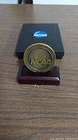 Front of the 2017 NCAA Division III East Regional NCAA medal on a wooden stand with black presentation box in the background