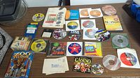 Top-down photo of various PC software and game discs, floppy disks, and cases laid out on a table. Includes Zoo Tycoon, Norton, Quicken, and multiple other titles.