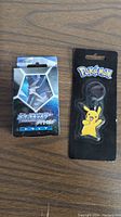 Photo showing the sealed Pokémon playing card set and Pikachu keychain on a wooden surface.