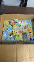 Cardboard box filled with stacks of loose Pokémon cards, random cards on top.