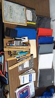 Overview of various school and office supplies arranged on a table including notebooks, rulers, pens, calculator, stapler, and binders.