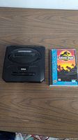 Sega Genesis console and Jurassic Park Sega CD game side by side on wood surface