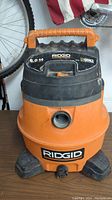 Front view of RIDGID shop vacuum showing brand, model capacity (6.0 gallons), hose port, and power on/off switch.