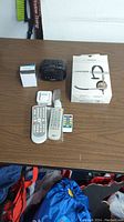 Photo of all seven electronic items including headset box, remotes, and Capello device on table.