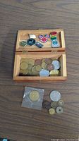 Wooden box containing assorted tokens and pins, some tokens outside the box including one in plastic sleeve.