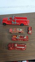 Four vintage fire truck toys on wood surface showing various sizes and details of each truck
