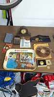 Photo of vintage lot items on a wooden surface including clock, calculator, tray, watch, tape reel and other items