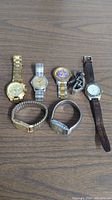 Seven vintage watches side by side on wooden surface showcasing variety of styles and bands.