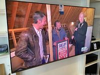 TV wall-mounted, powered on showing a program, slim black bezel