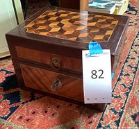 Closed hinged wooden box with geometric parquet inlay on lid and front, key in lock