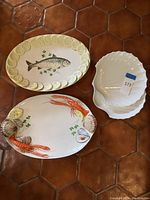 Three platters: Italian fish plate with lemon slices, Italian lobster plate with lemon slices and seashells, and white shell-shaped Japanese platter.