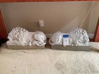 Both lions side by side on grey bases in front of a console table