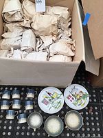 Box containing wrapped dishes with several blue speckled tea cups and a few decorative plates visible on top