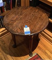 Circular wooden table measuring about 25 inches diameter and 24 inches tall. Visible wood grain on top, four turned legs with claw feet.