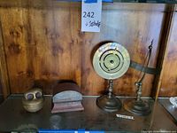 Photo showing metal owl figurine, metal box, and bronze dial sculpture on a wood shelf