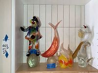 Shelf displaying five blown glass sculptures: clown, orange fish, two angel fish, tropical bird