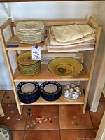 Wooden folding bookshelf displaying assorted dishes and linens across three shelves.