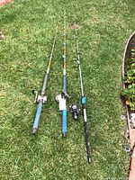 Three fishing rods laid out on grass, showing length and overall appearance.