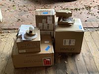 Grouped boxed light fixtures on wooden floor, multiple brands visible