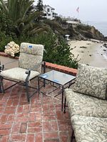 Photo showing two cushioned chairs and part of loveseat on brick patio overlooking ocean.