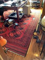 Full view of red and black Persian rug under desk showing overall pattern and wear