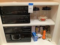 Four Pioneer stereo components stacked on shelves including receiver, equalizer, cassette deck, and CD player along with plastic cannisters, soup cup, flashlight, light bulbs and small repair parts.