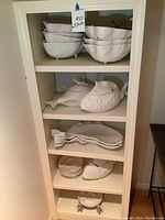 Shelf with multiple white ceramic serving bowls stacked: shell shaped bowls and fish shaped bowls with fish details