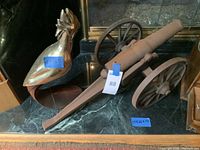 Photo showing the small heavy iron cannon and bird sculpture side by side on a marble surface with a fireplace in the background. Both items have size labels visible.