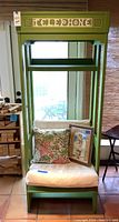 Front view of green telephone booth chair with seat cushion, throw pillow, and framed art leaning on seat.