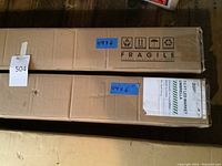 Two long rectangular cardboard boxes on the floor with dimensions labeled 49x6, marked fragile, containing the umbrellas.