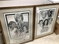 Both framed posters leaning against a wall, showing front view and overall condition.