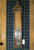 Full front view of carved wood barometer on tartan backdrop