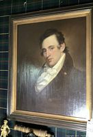 Full view of oil portrait painting in a dark wood frame with gold inner border against plaid background