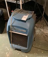 Front-three-quarter view of blue and gray dehumidifier showing air intake grille, molded handles, power cord and drain hose