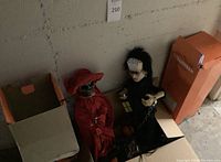 Wide view of two Halloween figures in cardboard boxes against concrete wall