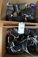 Photo showing multiple rolled leather and other material fashion belts of various styles and colors, mostly in black and brown, inside a cardboard box.