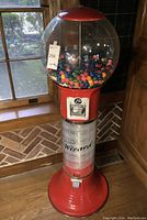 Full view of red metal base, clear cylinder and globe filled with gumballs