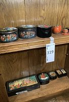 Shelf view of two painted Russian lacquer oval boxes, one plain black oval lacquer box and two ceramic tomato-shaped Limoges boxes.