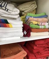 Photo showing folded towels including white towels with colored stripes, solid red and orange towels, and pastel colored towels.