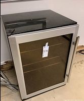 Front view of small refrigerator showing glass door with silver metal frame and handle.