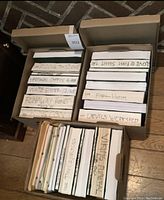 Three cardboard boxes holding loose stacks of typed scripts with handwritten spine labels on table
