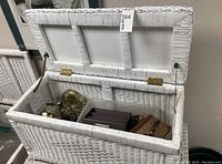 Open white wicker trunk showing brass hardware and interior contents