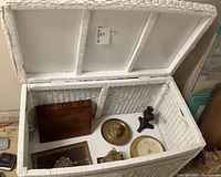 Wide top view of white wicker trunk open to show content items inside including boxes, plaques, and barometer.