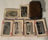 Photo of playing cards face up showing aces of hearts, spades, clubs, diamonds, title card, joker card, and leather carrying case.
