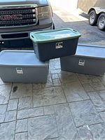 Three storage bins displayed outside on textured concrete. Two larger light gray bins and one smaller dark gray bin stacked on top, each with lids.
