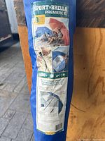 Blue Sport-Brella Premiere XL umbrella in a matching blue carrying bag with label showing product features and images of use at the beach.
