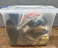 Plastic bin filled with assorted pens, markers, glue sticks, and other small office items