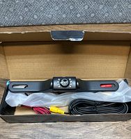 Top view of the black car rear view camera mounted on license plate bracket inside an open box showing cables and connectors.