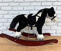 Side view of the black and white plush rocking horse on wooden rockers with saddle and stirrups.